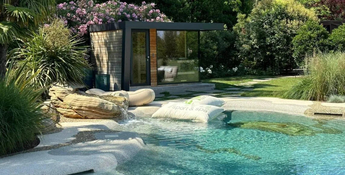 Lush poolside with a cabana, planting and a stone waterfall