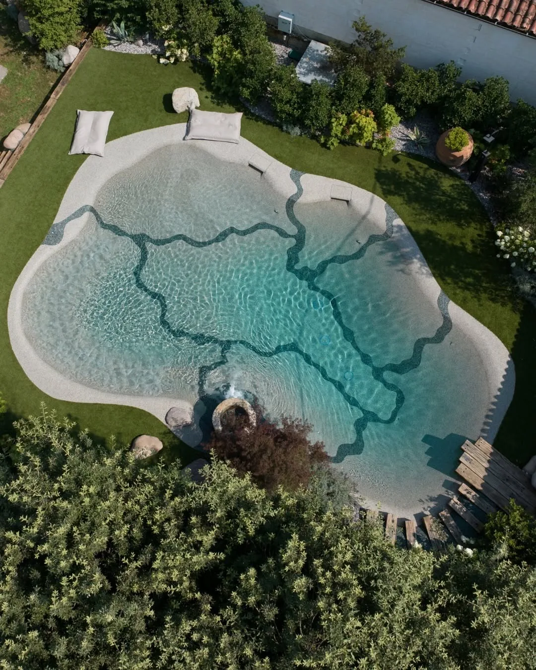 Aerial view of a beach-style pool with organic veined shallows, set into a green garden